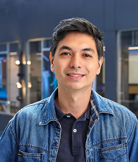 Man smiling in a denim jacket and dark polo shirt.