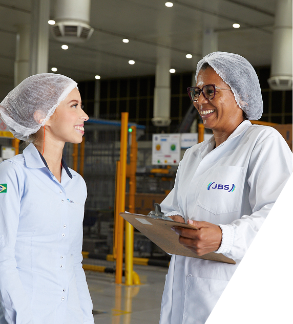 Two JBS employees smiling and talking in a factory setting.